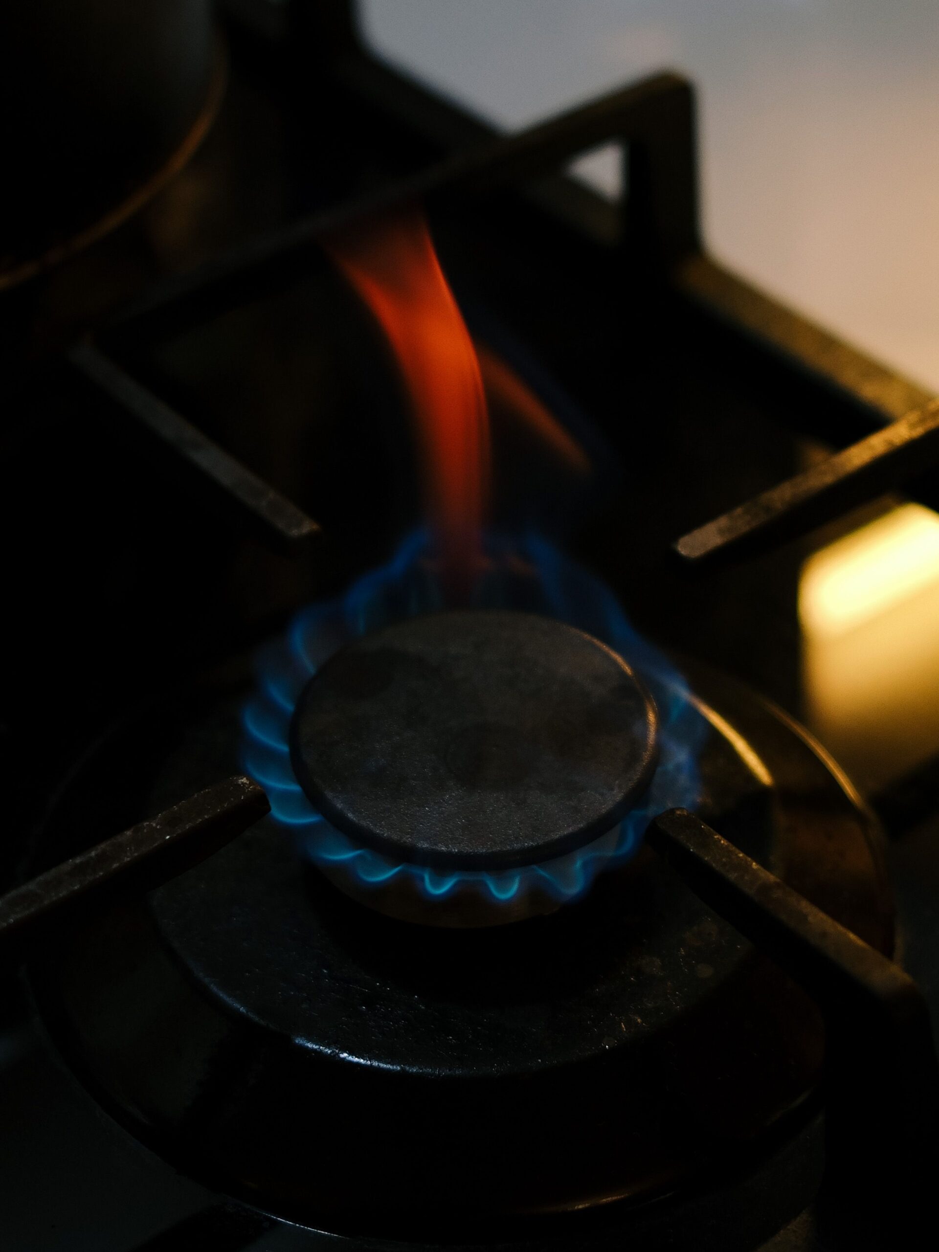 A close-up view of a lit gas stove burner with blue and red flames emanating from it.