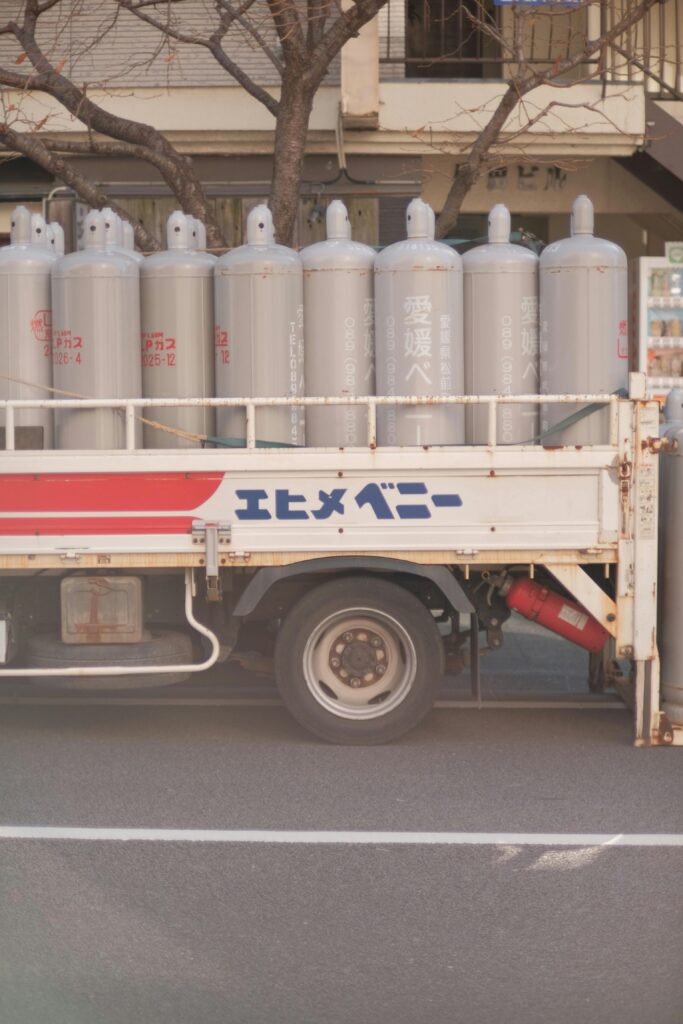Side view of a truck loaded with industrial gas cylinders parked on a city street.